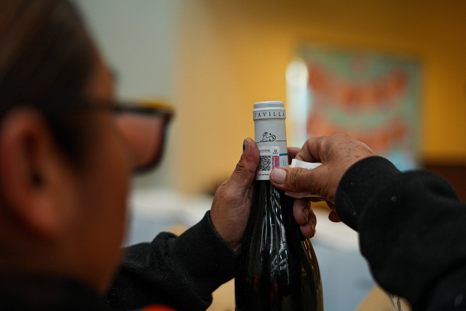Colaborador de Alminter colocando un marbete del SAT en el cuello de una botella de vino importado